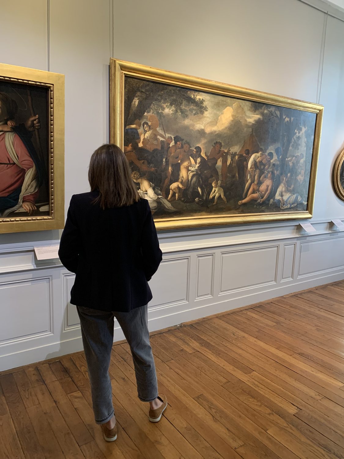 Fleur de dos, devant un grand tableau ancien dans un musée.